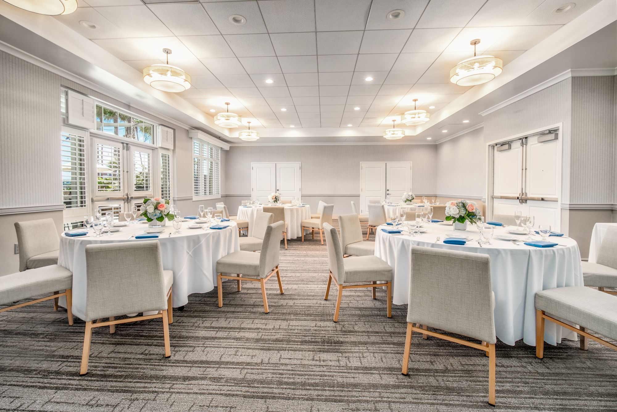 A conference banquet room set up for a meal: round tables with white tablecloths, place settings, chairs, and soft overhead lighting.