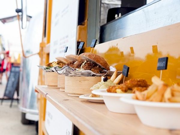 A food truck serving burgers and sides on a sunny street, with buns, fries, and dipping sauces displayed on a wooden counter. end.