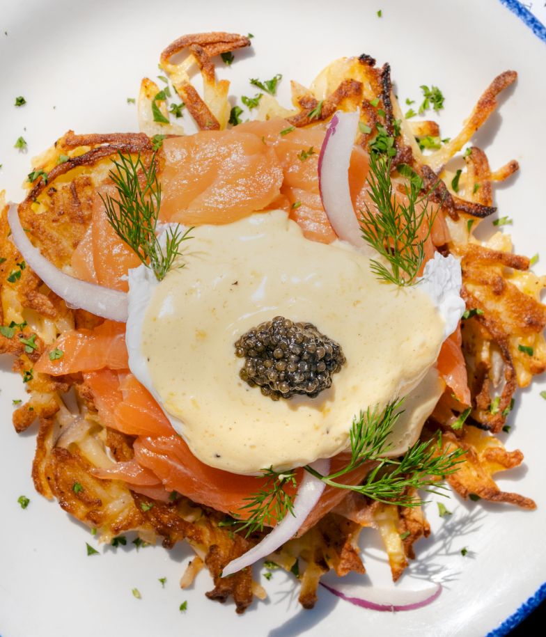 A plate of crispy potatoes topped with smoked salmon, onion slices, dill, a creamy sauce, and a dollop of caviar on top.